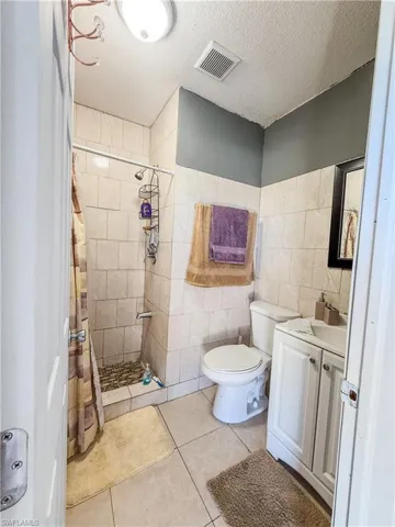 Bathroom featuring a tile shower, tile patterned flooring, vanity, tile walls, and visible vents