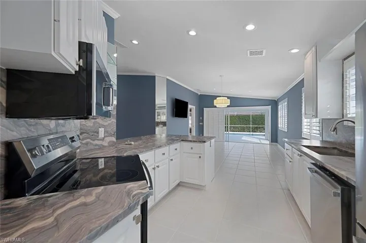 Kitchen featuring kitchen peninsula, appliances with stainless steel finishes, sink, white cabinetry, and hanging light fixtures