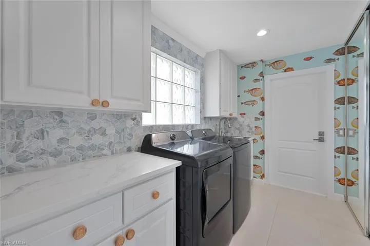 Clothes washing area with washer and clothes dryer, light tile patterned flooring, and cabinets