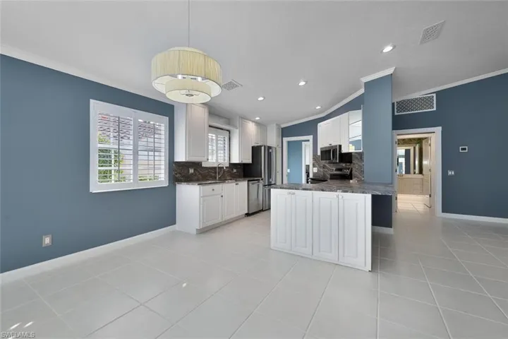 Kitchen with kitchen peninsula, decorative backsplash, stainless steel appliances, light tile patterned floors, and white cabinetry