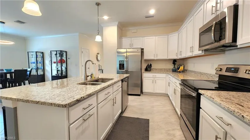 Kitchen featuring stainless steel appliances, a center island with sink, sink, light tile patterned floors, and crown molding