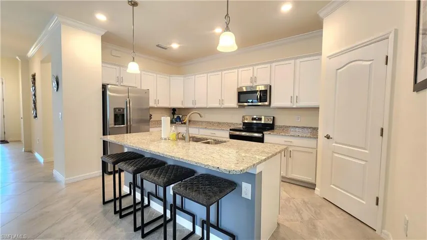 Kitchen featuring stainless steel appliances, sink, decorative light fixtures, light tile patterned floors, and white cabinetry