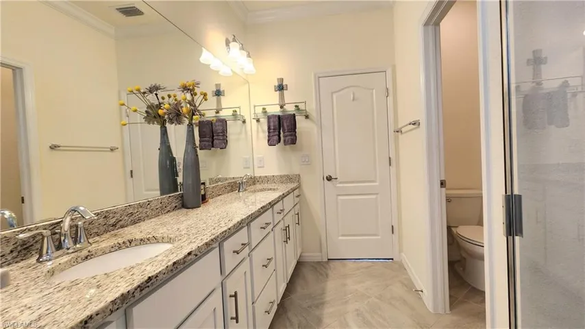 Bathroom with double vanity, tile patterned flooring, crown molding, and toilet