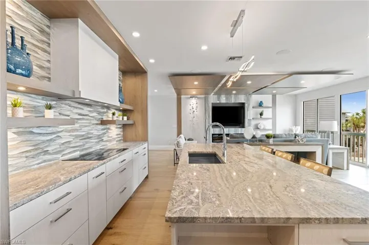 Kitchen with open shelves, a large island, light stone countertops, white cabinets, and modern cabinets