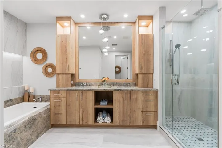 Bathroom featuring double vanity, a stall shower, light marble finish floors, a tub with marble appearance, and recessed lighting