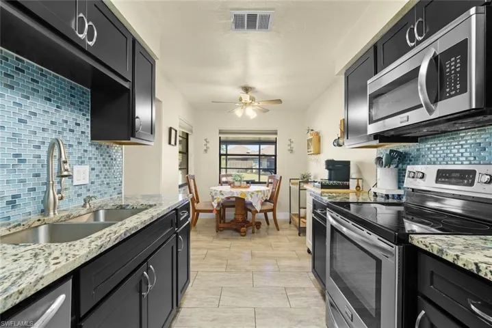 Kitchen with light stone counters, sink, stainless steel appliances, and ceiling fan