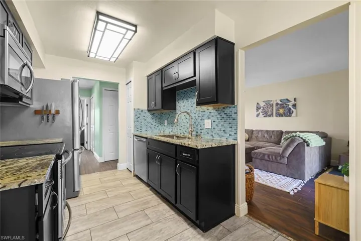 Kitchen with light stone counters, sink, backsplash, and stainless steel appliances