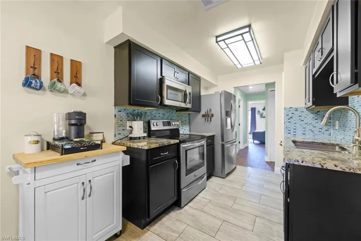 Kitchen with tasteful backsplash, stainless steel appliances, sink, and light stone counters