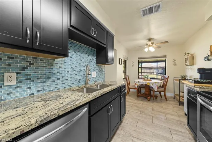 Kitchen featuring sink, ceiling fan, appliances with stainless steel finishes, tasteful backsplash, and light stone countertops