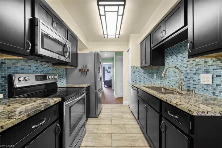Kitchen featuring appliances with stainless steel finishes, sink, light stone counters, and decorative backsplash