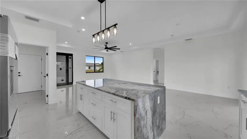 Kitchen featuring white cabinets, ceiling fan, hanging light fixtures, light marble finish floors, and recessed lighting