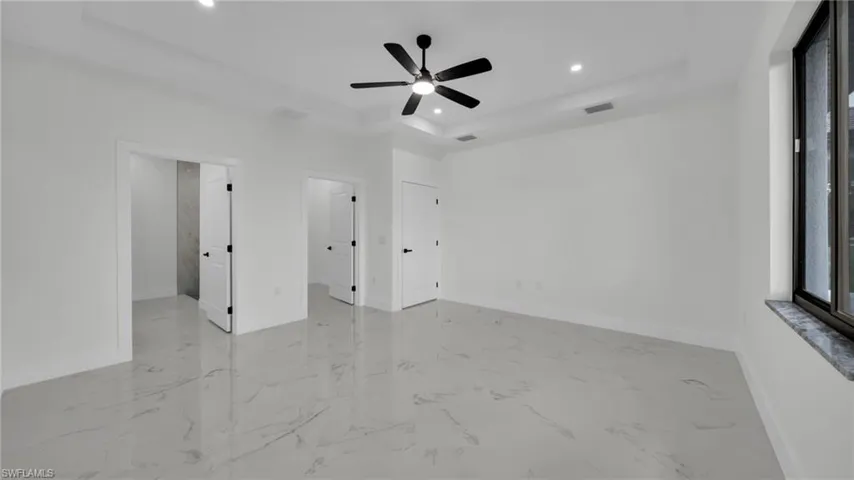 Unfurnished bedroom featuring a raised ceiling, light marble finish floors, a ceiling fan, and recessed lighting