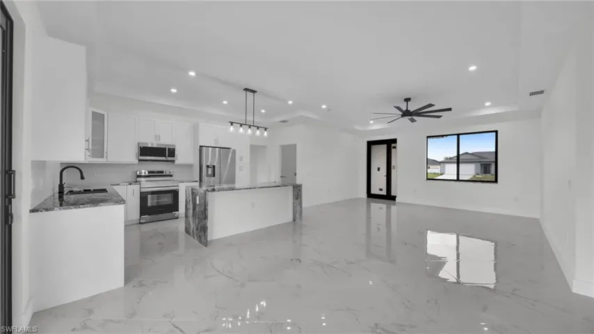 Kitchen featuring a kitchen island, dark stone counters, white cabinetry, a tray ceiling, and hanging light fixtures
