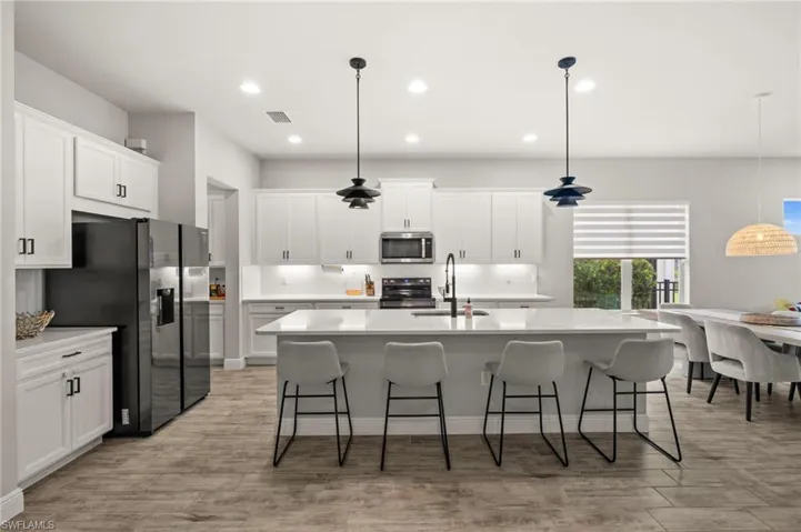Kitchen featuring black appliances, hanging light fixtures, an island with sink, white cabinets, and a kitchen breakfast bar