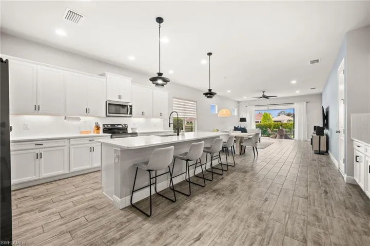 Kitchen featuring white cabinets, backsplash, a kitchen bar, a center island with sink, and a ceiling fan