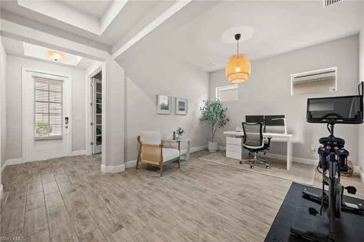 Spacious room featuring wood-finish tile flooring throughout, a front entry with a transom window and blinds, and a built-in light fixture