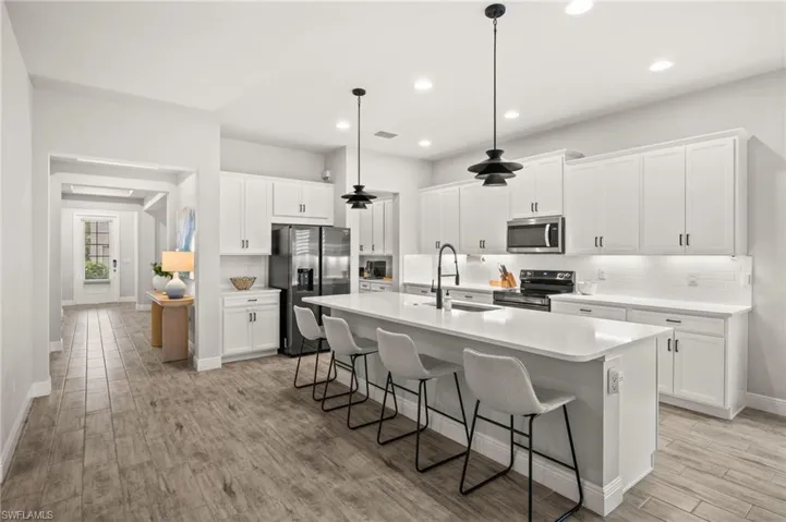 Kitchen featuring a breakfast bar area, range with electric cooktop, refrigerator with ice dispenser, a center island with sink, and white cabinets
