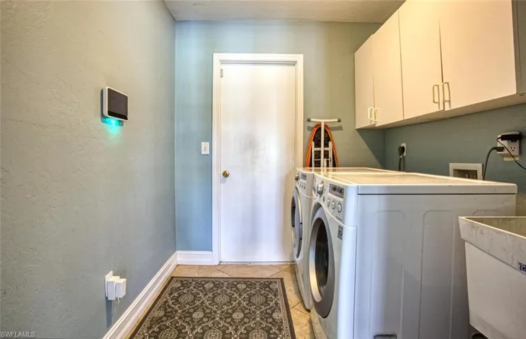 Laundry room with a textured wall, light tile patterned floors, cabinet space, and independent washer and dryer
