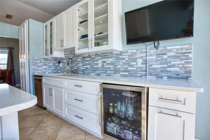 Bar area featuring wine cooler, white cabinets, light stone counters, and glass fronted cabinets