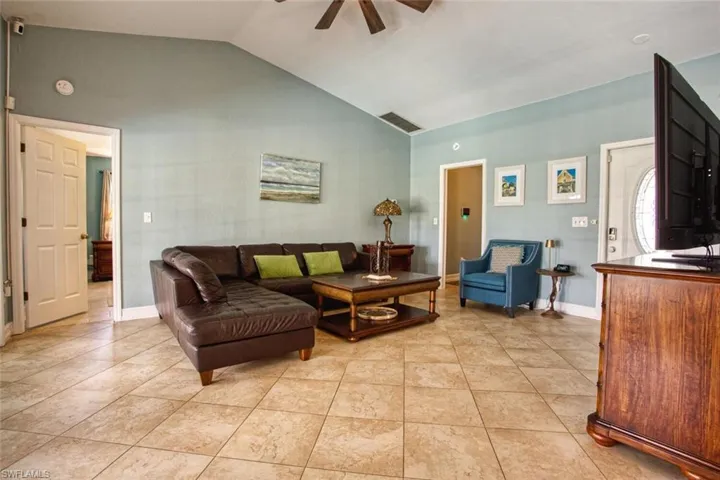 Living room featuring lofted ceiling, a ceiling fan, and light tile patterned flooring