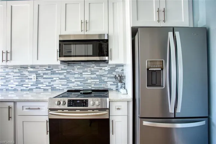 Kitchen featuring stainless steel appliances, white cabinets, light stone countertops, and decorative backsplash