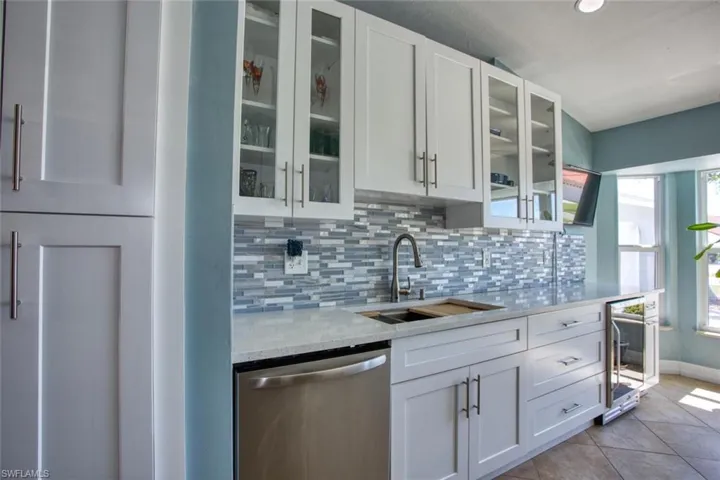 Kitchen with glass insert cabinets, white cabinets, dishwasher, light stone countertops, and recessed lighting