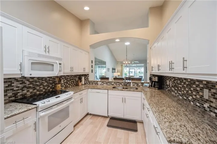 Kitchen with backsplash, white cabinetry, a chandelier, and white appliances