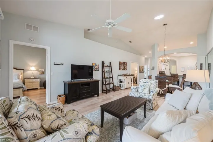 Living room with arched walkways, light wood-style floors, vaulted ceiling, ceiling fan with notable chandelier, and visible vents
