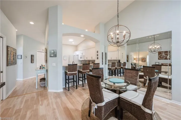 Dining room featuring light wood-style flooring, a notable chandelier, baseboards, arched walkways, and high vaulted ceiling