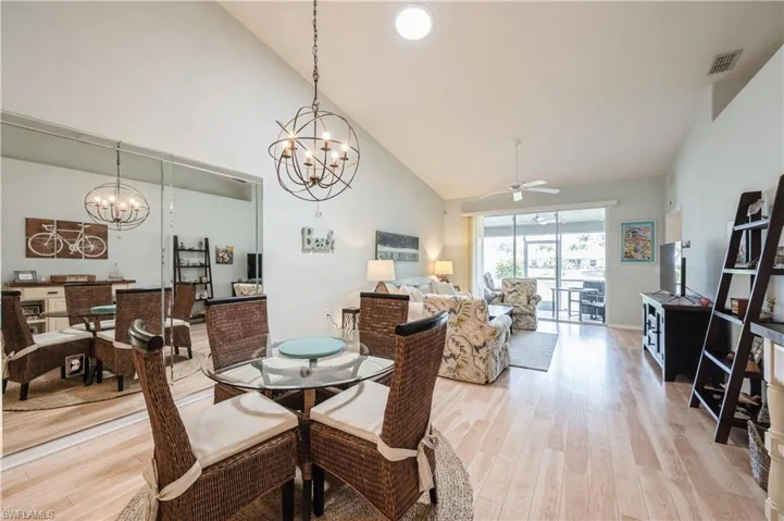 Dining area with ceiling fan with notable chandelier, high vaulted ceiling, visible vents, and light wood-style floors