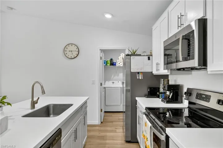 Kitchen with stainless steel appliances, washer / dryer, light wood finished floors, light countertops, and white cabinets
