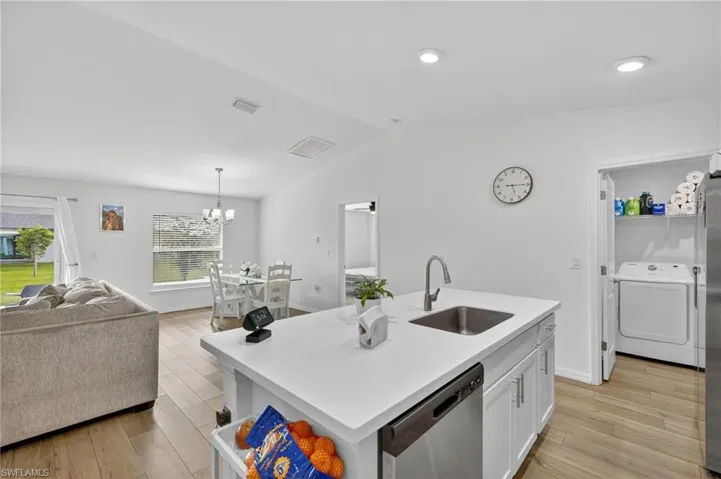 Kitchen featuring washer / dryer, dishwasher, open floor plan, white cabinetry, and light wood-type flooring