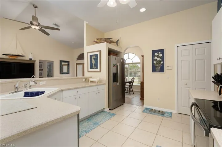 Kitchen featuring a ceiling fan, stainless steel refrigerator with ice dispenser, a sink, arched walkways, and high vaulted ceiling