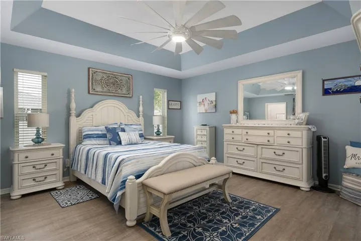 Bedroom featuring wood finished floors, a tray ceiling, baseboards, and a ceiling fan