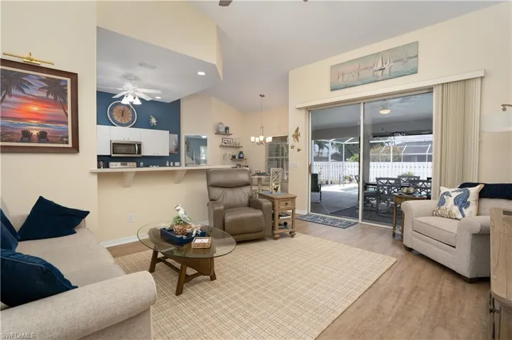 Living area featuring ceiling fan, light wood-style flooring, high vaulted ceiling, a chandelier, and baseboards