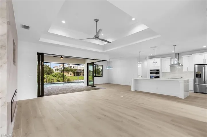 Unfurnished living room featuring light wood-style floors, a tray ceiling, a ceiling fan, and recessed lighting