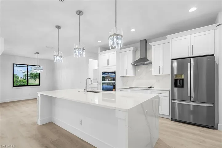 Kitchen featuring black appliances, light stone counters, wall chimney range hood, decorative backsplash, and white cabinets