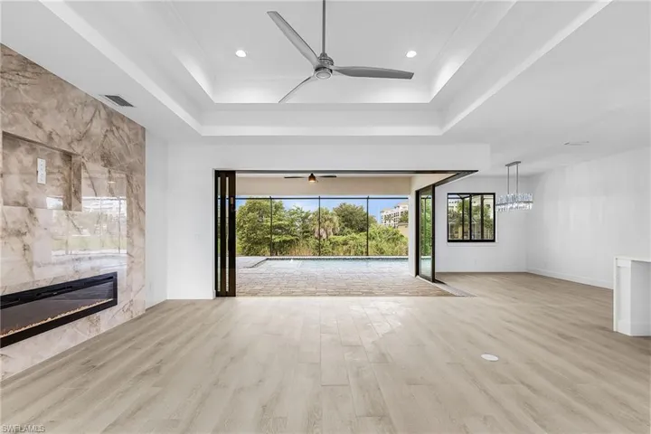 Unfurnished living room featuring light wood-type flooring, ceiling fan, a fireplace, recessed lighting, and a raised ceiling