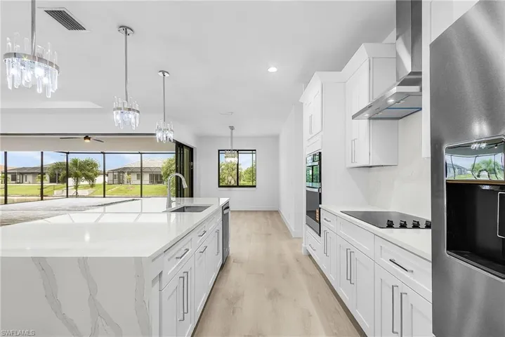 Kitchen featuring appliances with stainless steel finishes, white cabinetry, wall chimney range hood, light stone countertops, and light wood-style floors