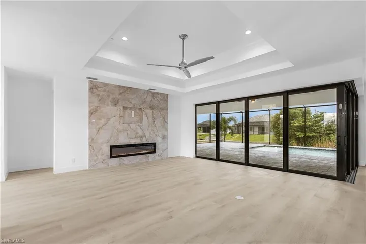 Unfurnished living room featuring light wood-style floors, a premium fireplace, a ceiling fan, a raised ceiling, and recessed lighting