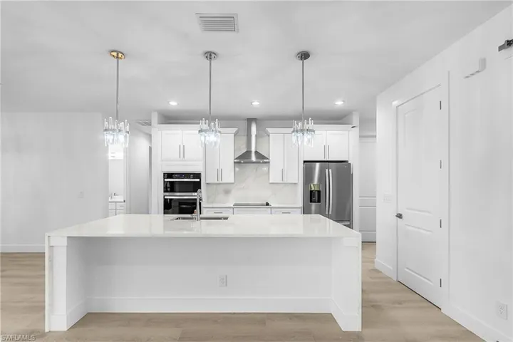 Kitchen featuring white cabinets, light stone countertops, stainless steel appliances, backsplash, and light wood-type flooring