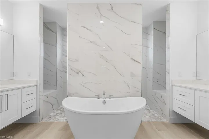 Master Bathroom featuring vanity, a freestanding bath, light wood-style flooring, dual shower entrance, and tile walls