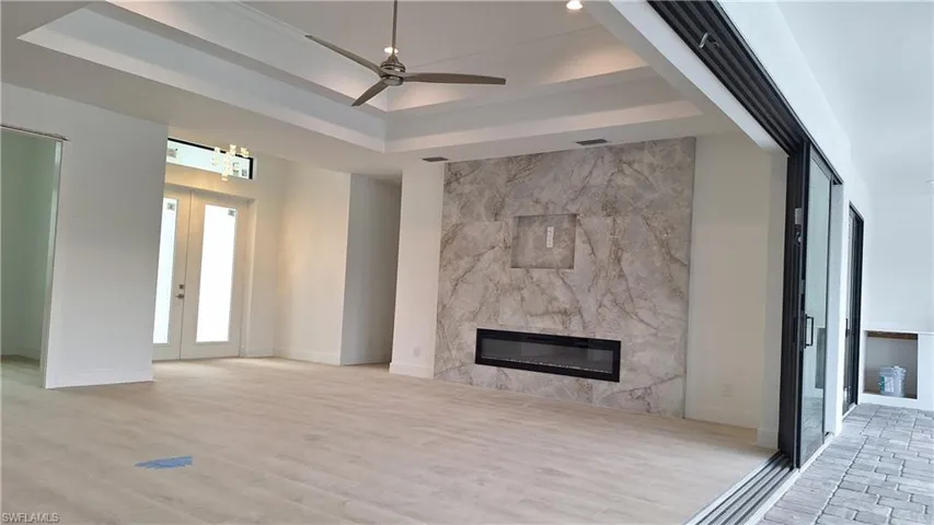 Unfurnished living room featuring a raised ceiling, a high end fireplace, light wood-style floors, ceiling fan, and french doors