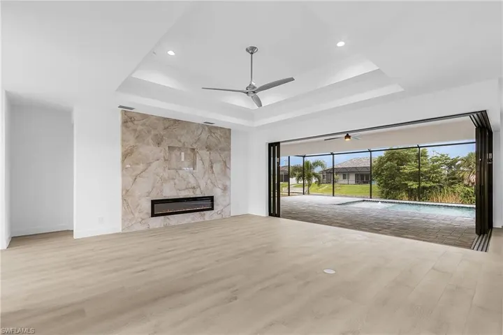 Unfurnished living room featuring light wood finished floors, a sunroom, a high end fireplace, a tray ceiling, and recessed lighting