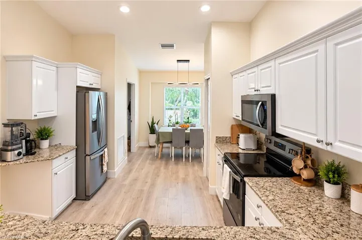Kitchen featuring white cabinetry, granite countertops, stainless steel appliances, and wood-finish flooring