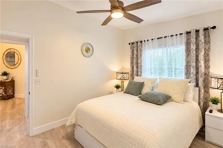 Wood-finish flooring throughout, ceiling fan with integrated lighting, window with blinds and decorative drapery, and a neutral wall color