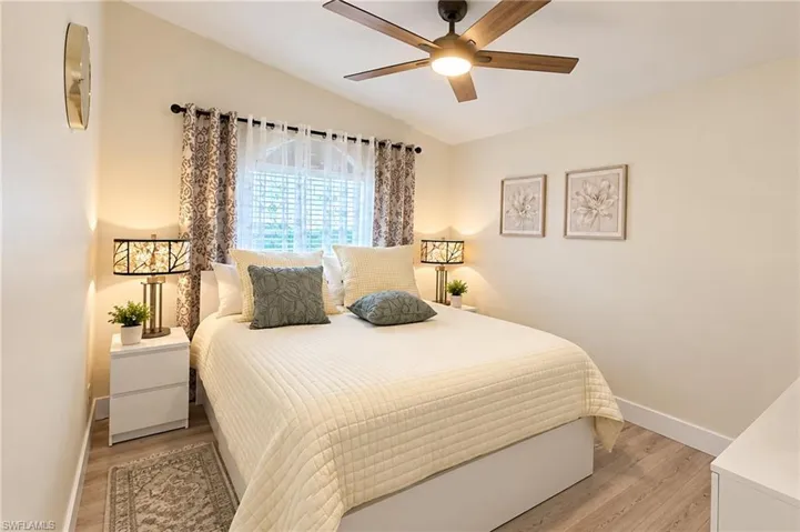 Vaulted ceiling featuring a ceiling fan with integrated lighting, arched window with plantation shutters, wood-finish flooring, and white baseboards