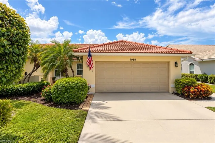 Terracotta tile roof, attached garage, exterior wall sconce, concrete driveway, and mature landscaping