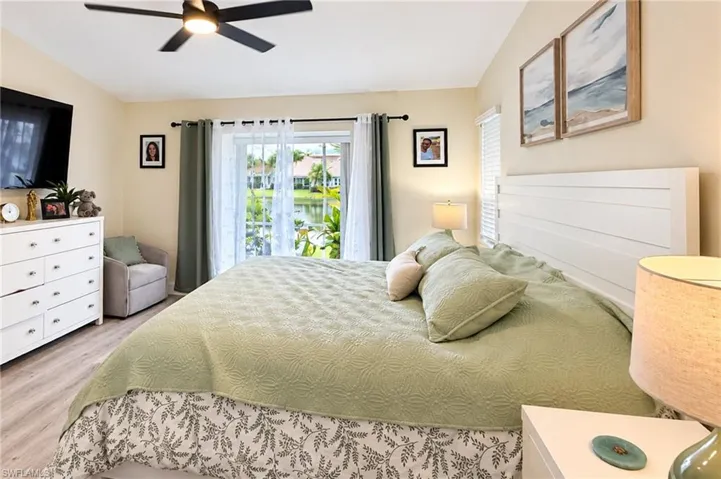 Sliding glass doors, a ceiling fan with integrated lighting, wood-finish flooring, and a white paneled headboard