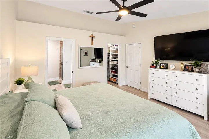 Light-toned walls with wood-finish flooring, a ceiling fan with integrated lighting, and a walk-in closet with built-in shelving